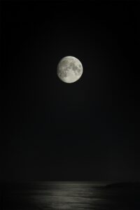 Full moon rising over calm coastal water at night