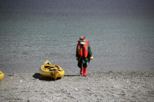 Young paddler in a life jacket walking toward a yellow kayak on the beach