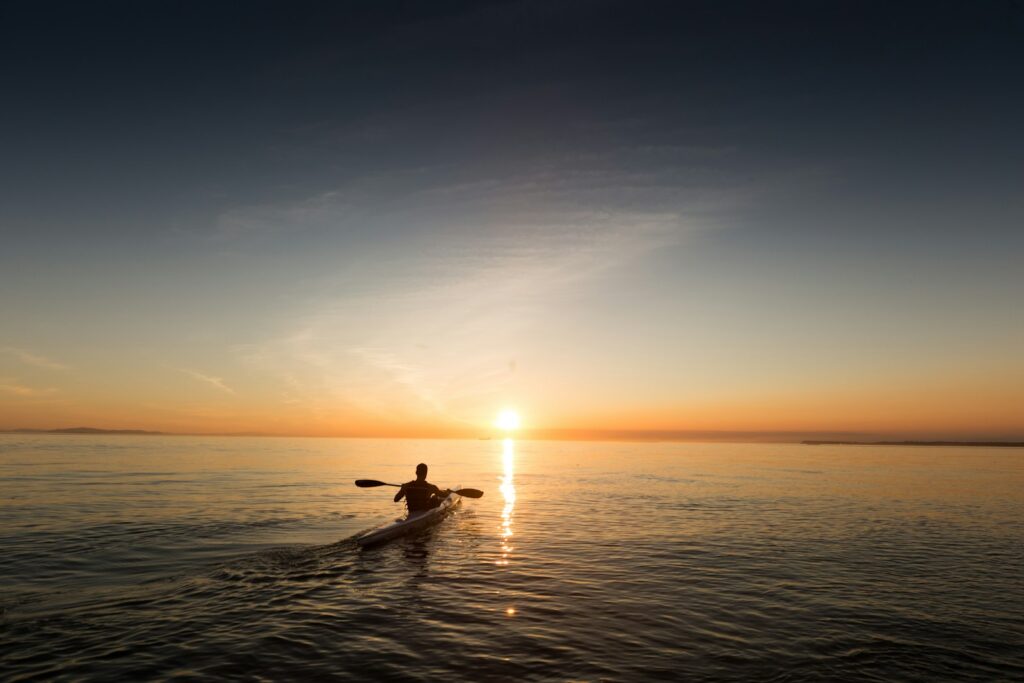 Kayaker paddling across calm water at sunset