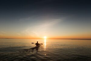 Kayaker paddling across calm water at sunset